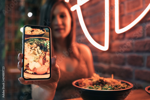 Unrecognizable young girl showing the camera the picture she just took with her mobile phone to her poke bowl.