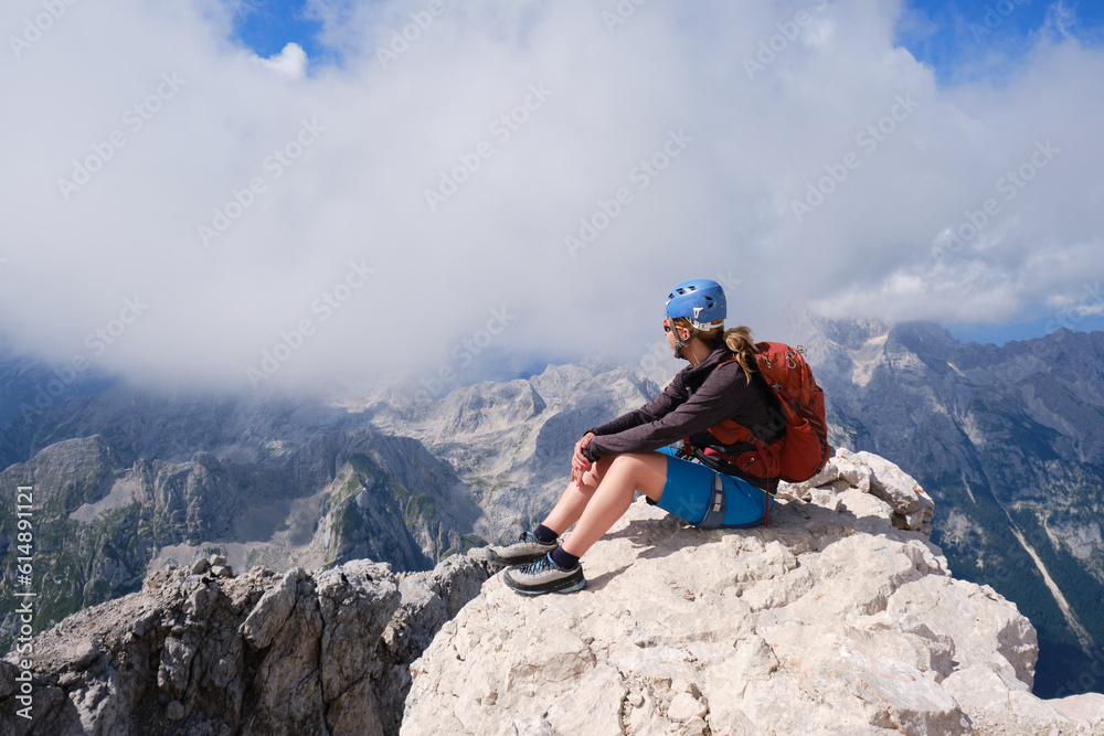 Woman climber sits on a rock at Triglav peak, Slovenia, on a Summer day. Adventure, active, summit, goal, activity, mountain, national park, trekking.