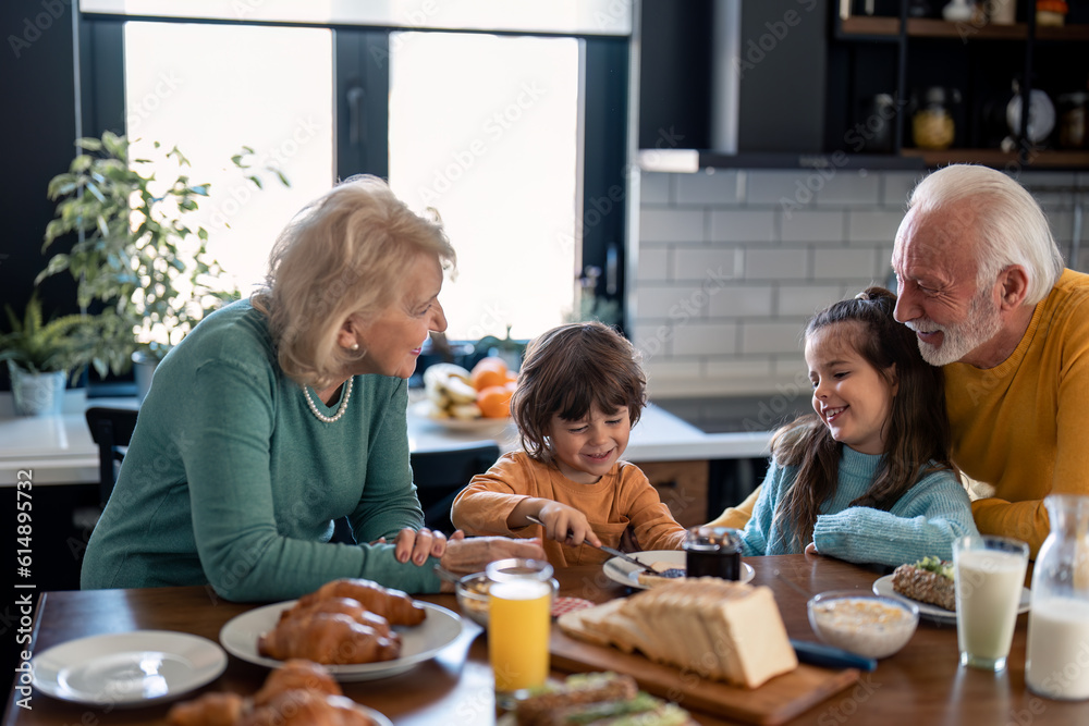 Satisfied smiling little boy spreading marmalade jam from jar on slice of bread for breakfast, enjoying family time with cute older sister and proud happy grandmother and grandfather. Satisfied smiling little boy spreading marmalade jam from jar on slice of bread for breakfast, enjoying family time with cute older sister and proud happy grandmother and grandfather.
