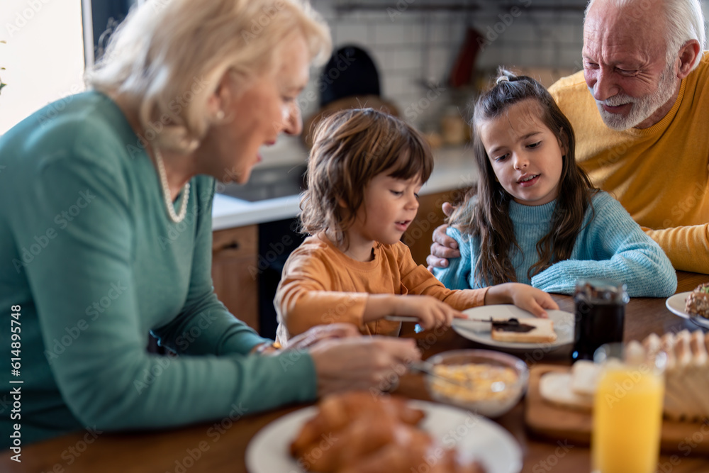 Senior woman and senior man having breakfast with two children at dinning table in the kitchen at home.