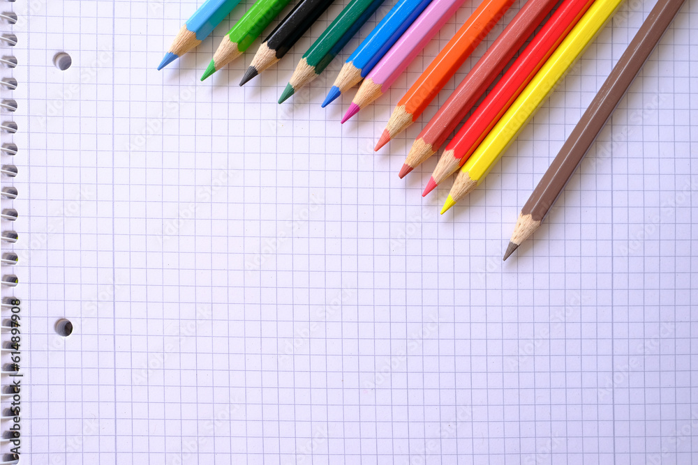 school background, colored pencils lie on a sheet of paper, an open notebook on a spiral, a college block in a cage, close-up, the concept of student writing supplies, back to school school background, colored pencils lie on a sheet of paper, an open notebook on a spiral, a college block in a cage, close-up, the concept of student writing supplies, back to school