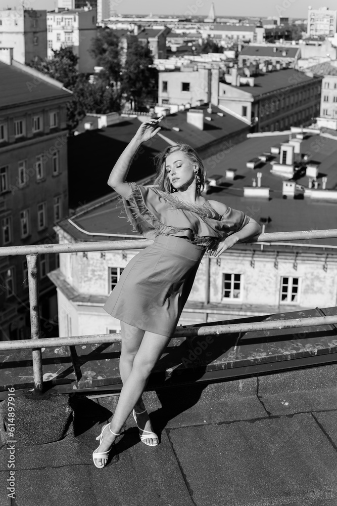 Obraz premium Elegant young lady in ruffle attire, heels shoes stand on rooftop leaning on fence with closed eyes and lifting arm. 