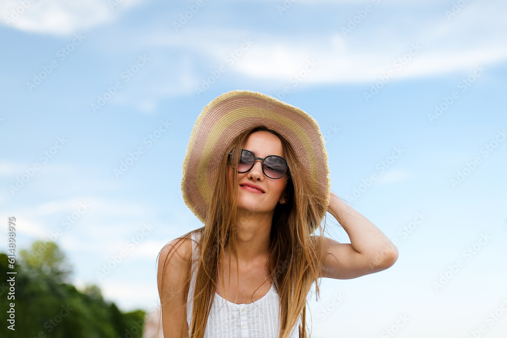 Happy smiling woman in free happiness bliss on ocean beach standing and posing with hat and sunglasses. Portrait of a female model in white summer dress enjoying nature during travel holidays vacation