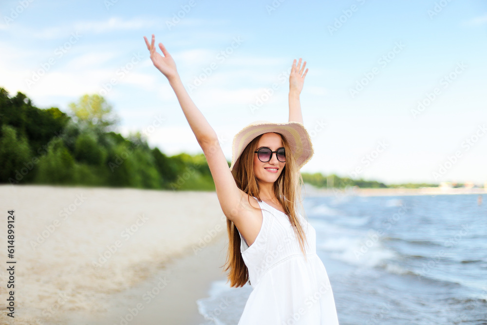 Happy smiling woman in free happiness bliss on ocean beach standing with a hat, sunglasses, and rasing hands. Portrait of a multicultural female model in white summer dress enjoying nature during Happy smiling woman in free happiness bliss on ocean beach standing with a hat, sunglasses, and rasing hands. Portrait of a multicultural female model in white summer dress enjoying nature during
