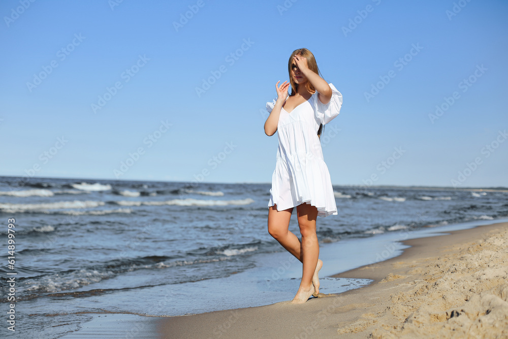 Happy smiling beautiful woman is walking on the ocean beach in a white summer dress Happy smiling beautiful woman is walking on the ocean beach in a white summer dress