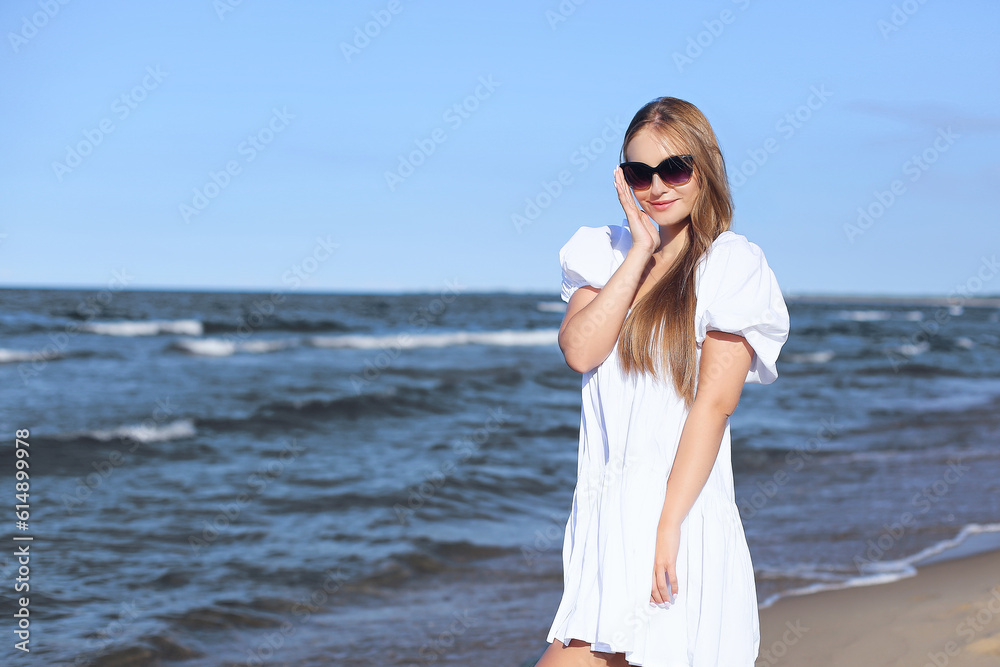 Happy smiling blonde woman is posing on the ocean beach with sunglasses Happy smiling blonde woman is posing on the ocean beach with sunglasses