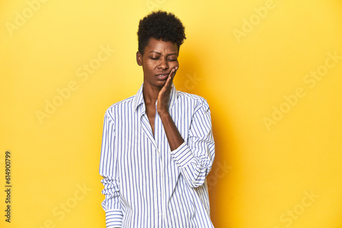 African businesswoman, blue striped shirt, yellow backdrop, having a strong teeth pain, molar ache.