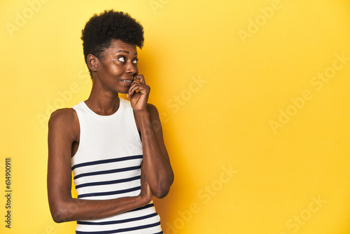 Vibrant African woman, white tank-top, yellow studio, relaxed thinking about something looking at a copy space.