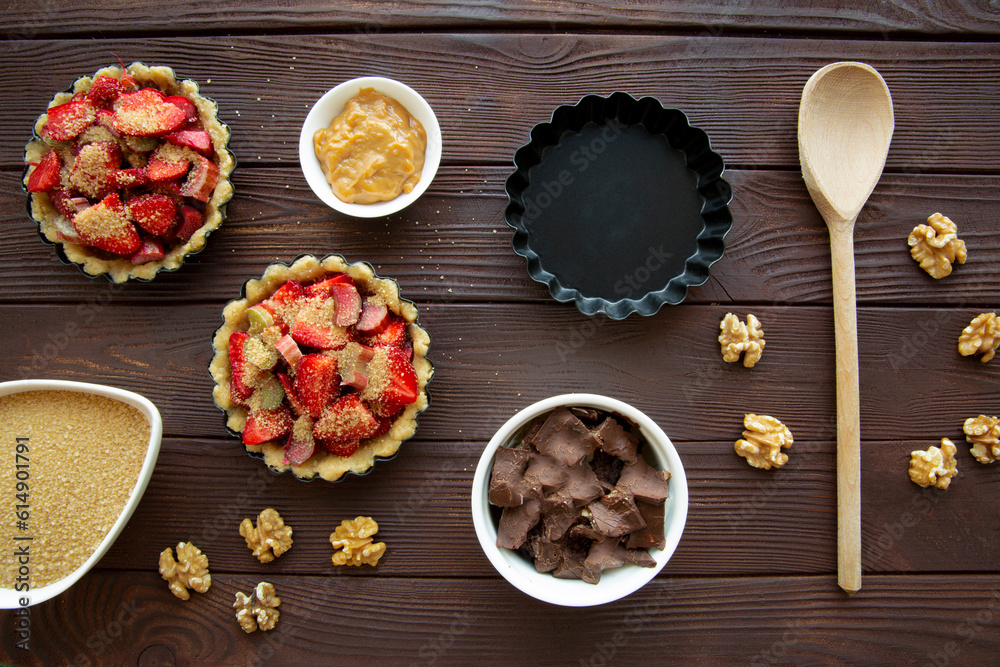 Mini tarts with strawberry, chocolate and nuts preparation on brown wooden table, top view. Mini tarts with strawberry, chocolate and nuts preparation on brown wooden table, top view.