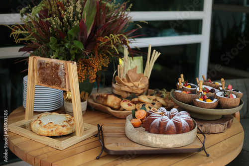 Linda mesa de brunch com uma variedade de pães, pastas, salada de frutas, queijos e bolo. Decorada com um belo arranjo de flores, em um evento diurno chique.