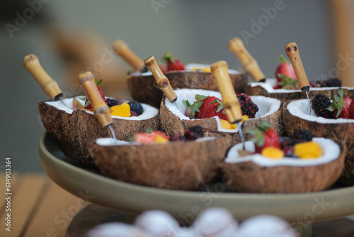 Salada de frutas servida em tigelas de coco, acompanhada por um garfo requintado de cabo de bambu, em um evento social chique.