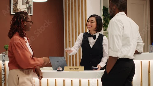 Rich tourists purchasing luxury ensuite hotel room at front desk reception using credit card. Company executives on business trip buying resort amenities from helpful receptionist photo