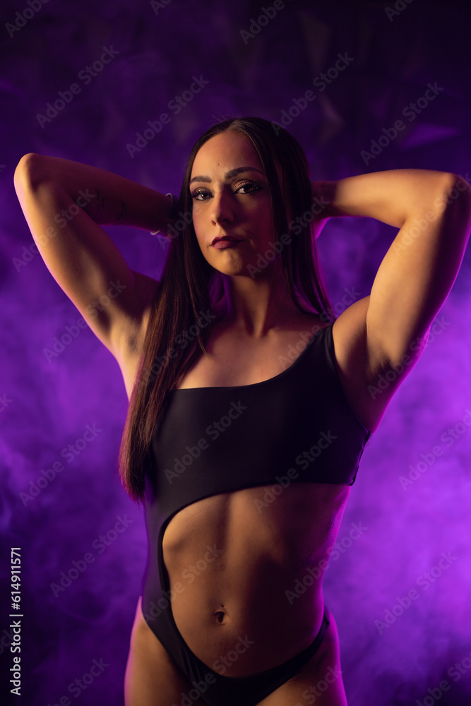 Obraz premium female fitness competitor posing in purple smoke