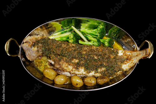 traditional french delicacy sole meuniere with green vegetables, potato and lemon capers butter in a copper pan with black background, similar to dover sole grenobloise