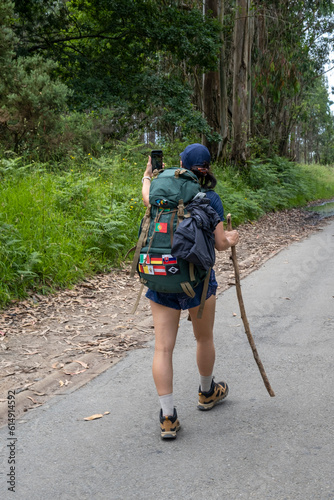 Young woman pilgrim taking a selfie on a trail of the way of saint james. Camino de Santiago. Vertical shot. photo