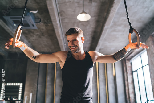 Strong male athlete standing with gymnastic rings in gym photo