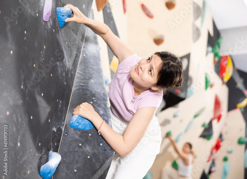 Young sports central asian woman training to climb wall on climbing wall