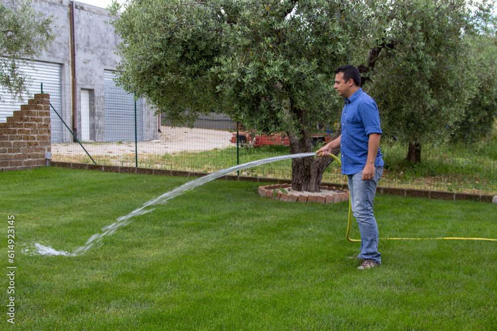 Image of a man watering his garden with a hose. Lawn care and maintenance and reference to water waste and drought.
