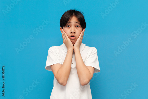 Φωτογραφία shocked asian schoolboy of twelve years old is surprised and worried on blue iso