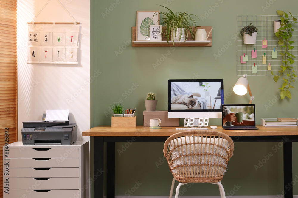 Fototapeta premium Stylish workplace with computer, laptop and lamp near olive wall at home