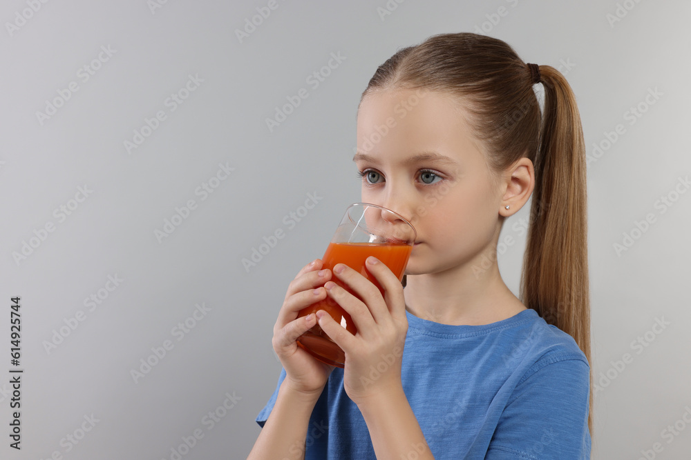 Cute little girl drinking fresh juice on light gray background, space for text Cute little girl drinking fresh juice on light gray background, space for text