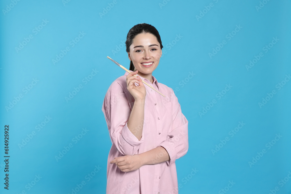 Woman with paintbrush on light blue background. Young artist Woman with paintbrush on light blue background. Young artist