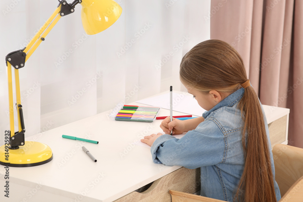 Cute little girl drawing with markers at desk in room. Home workplace