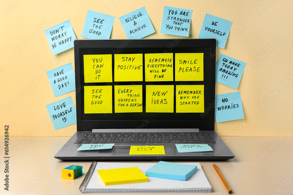 Paper notes with life-affirming phrases and laptop on table against beige background Paper notes with life-affirming phrases and laptop on table against beige background