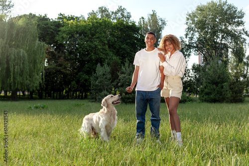 young african american couple with dog stand in park on green grass and smile