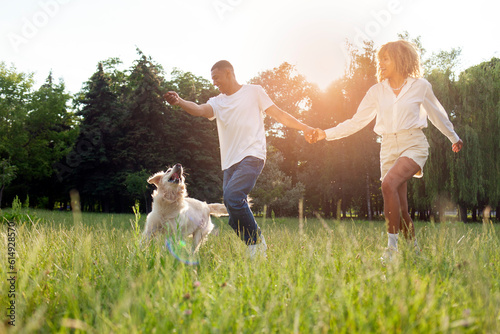 young african american couple play with dog in park on green grass and run