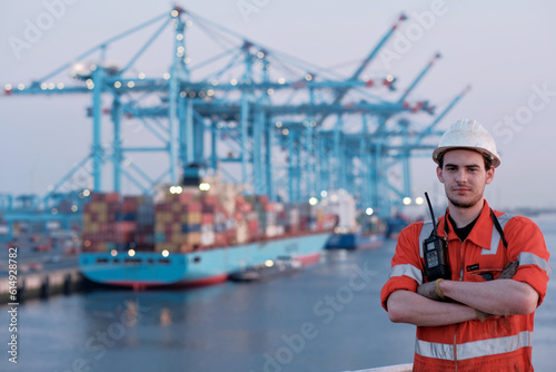 Offshore technician. Seafarer. Seaman. Navigator. A man in a boiler suit is standing in front of the port. Seafarer in front of the container terminal. photo