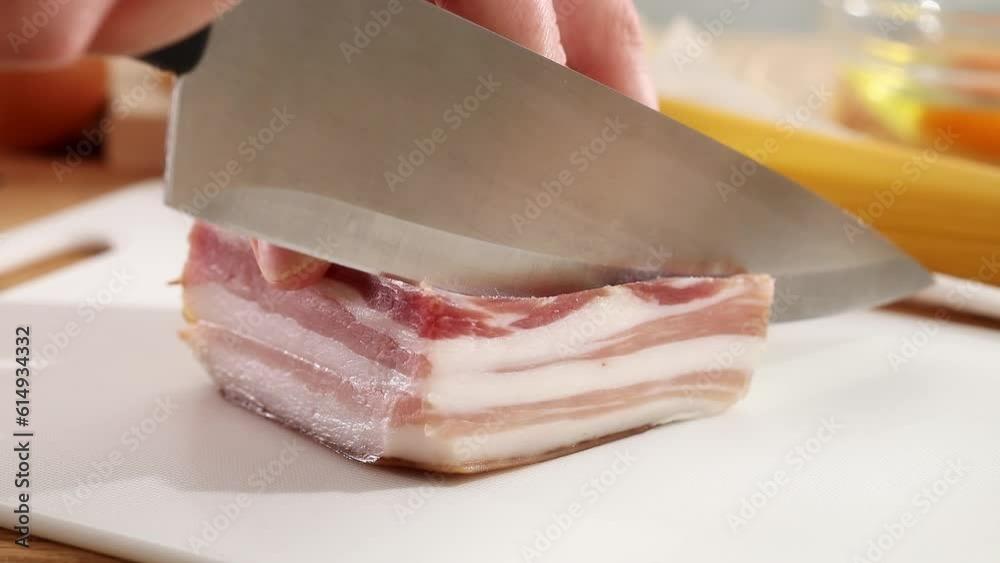Cutting pancetta with a knife on a cutting board. Ingredient for pasta carbonara. Cooking traditional Italian food. High quality 4k footage