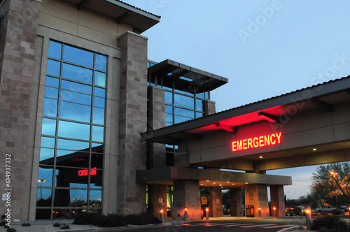 An illuminated red “Emergency” sign marks the entrance to a modern hospital emergency department at dusk, signaling urgent medical care access