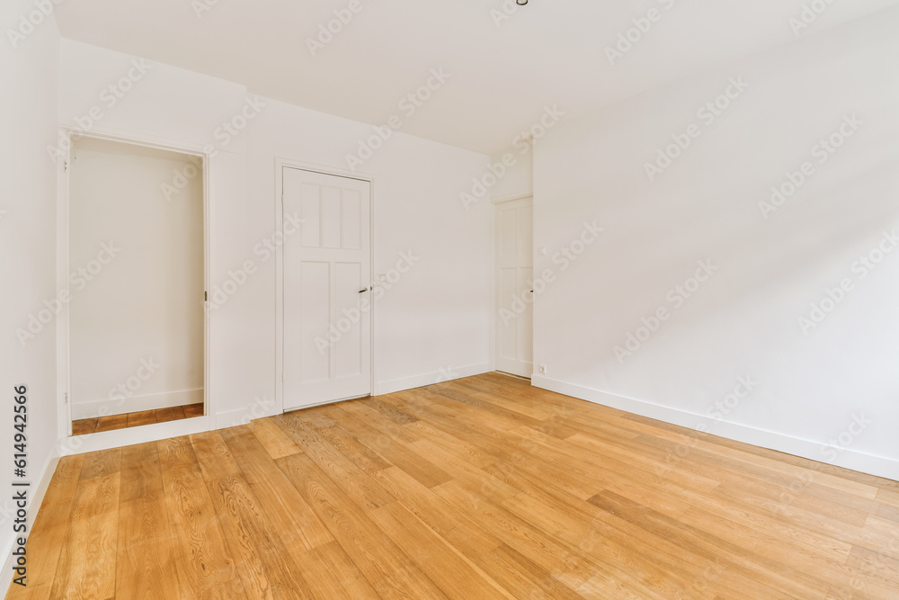 an empty room with white walls and wood flooring on one side, there is a door in the other corner an empty room with white walls and wood flooring on one side, there is a door in the other corner