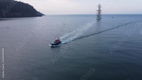 A large sail powered cruise ship is arriving in port, cutting to follow a pilot boat leading the way into Dartmouth, Devon, United Kingdom. photo