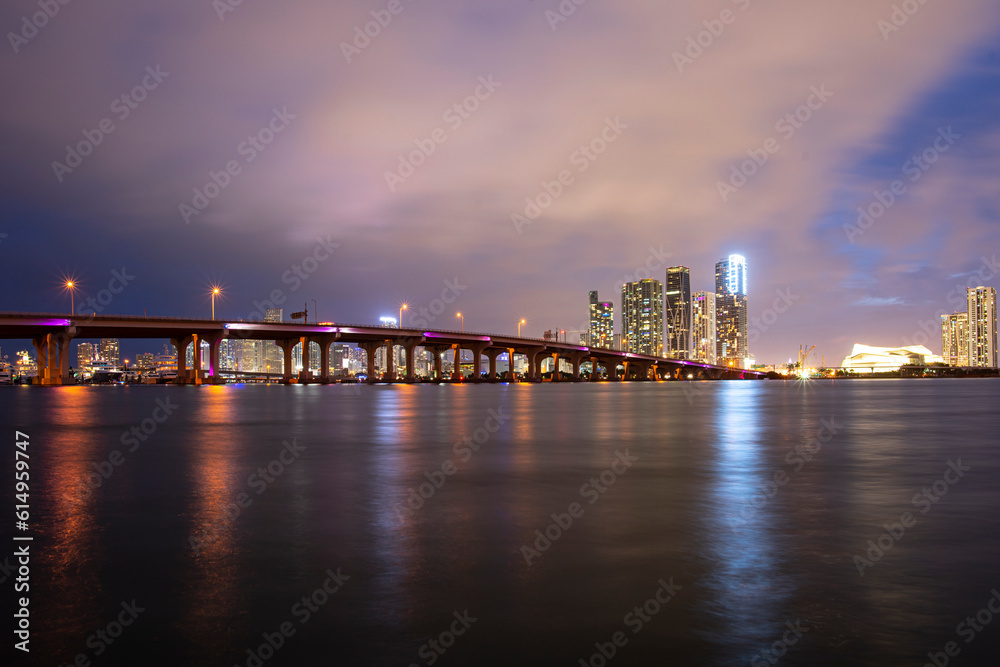 Miami city skyline panorama at night skyscrapers and bridge over sea with reflection