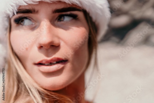 Fototapeta Naklejka Na Ścianę i Meble -  Woman summer travel sea. Happy tourist in red bikini and Santas hat enjoy taking picture outdoors for memories. Woman traveler posing on the beach surrounded by volcanic mountains, sharing travel joy