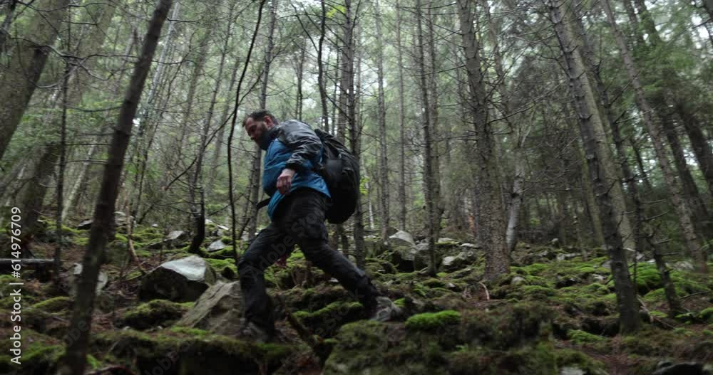 A young man in a mountain hiking with a backpack among the trees in a dense foggy forest. Single hike in long weather.