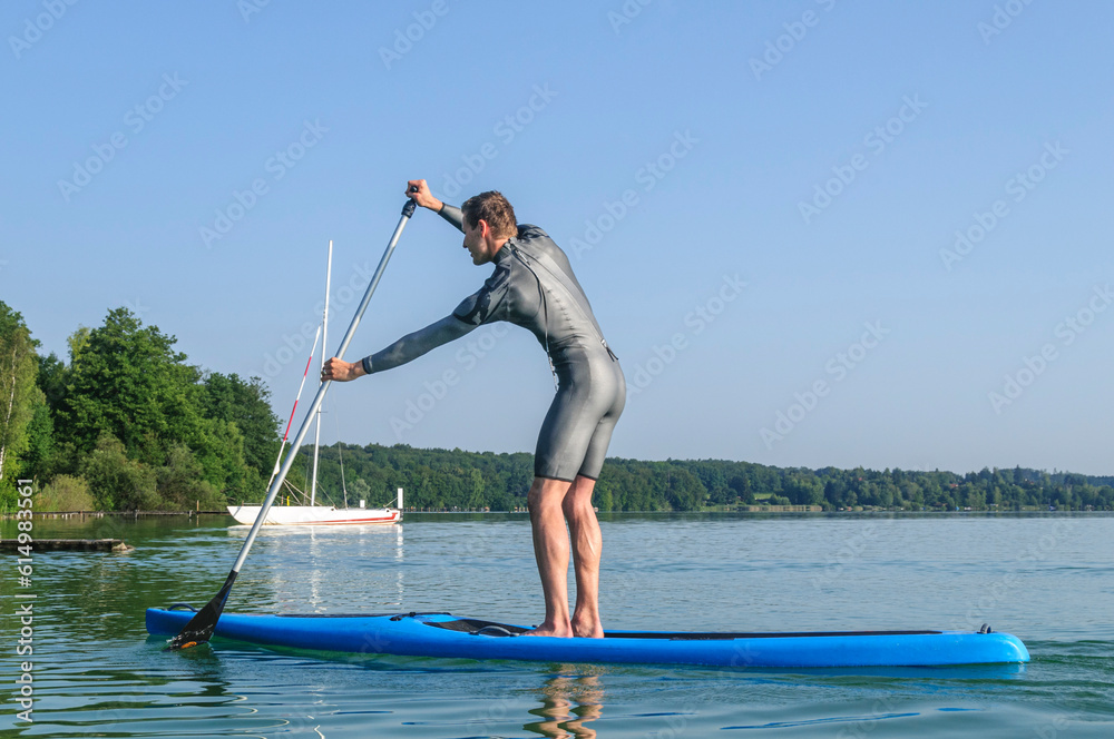 Naklejka premium Junger Mann hat Spaß bei einer SUP-Tour auf einem bayerischen See