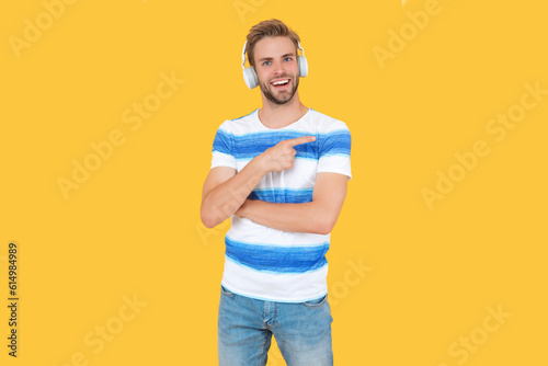 man listen and enjoys live music, point finger. man listens to music on headphones isolated on yellow. man relaxes and listens to music in studio. man uses his wireless headphones to listen to music