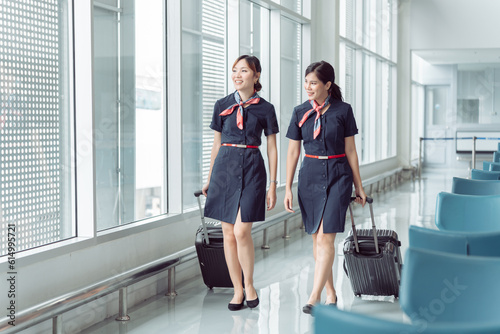 Two beautiful asian woman working in flight attendants in uniform dragging her luggage to airport terminal, people working together with teamwork in customer service. photo