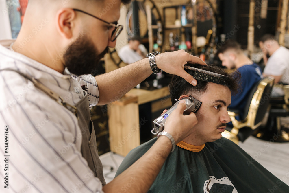 Handsome bearded man cutting hair of confident male client in berber shop Handsome bearded man cutting hair of confident male client in berber shop