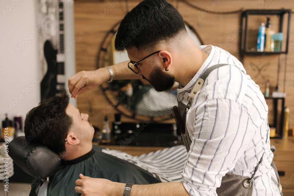 Process of threading procedure in barber shop. Professional barber correcting shape of brows with threads male client sitting in chair. Process of threading procedure in barber shop. Professional barber correcting shape of brows with threads male client sitting in chair.