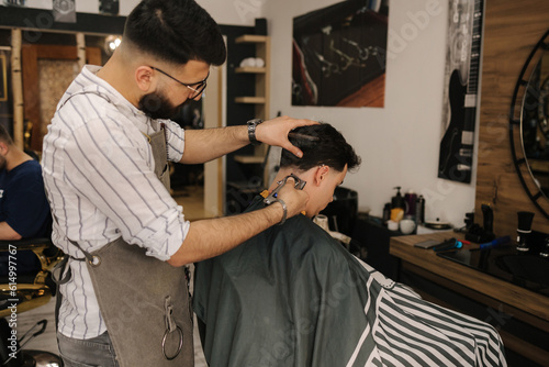 Handsome bearded man cutting hair of confident male client in berber shop