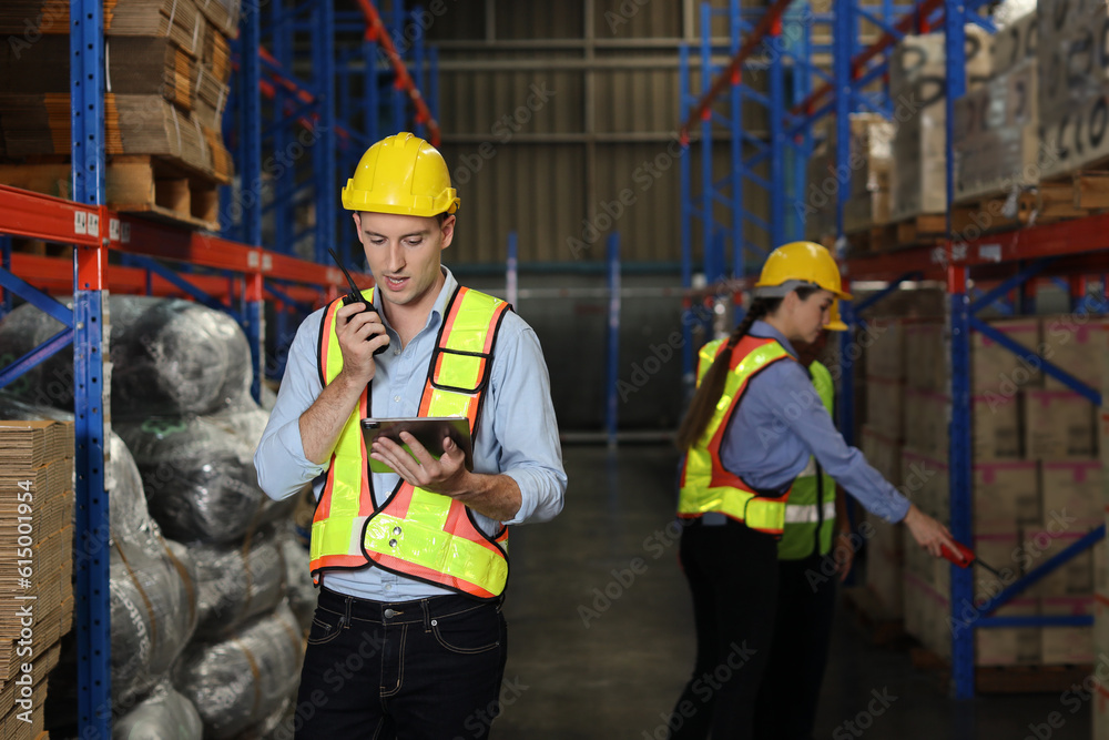 Group of warehouse workers with hardhats and reflective jackets using tablet, walkie talkie radio and cardboard while controlling stock and inventory in retail warehouse logistics, distribution center Group of warehouse workers with hardhats and reflective jackets using tablet, walkie talkie radio and cardboard while controlling stock and inventory in retail warehouse logistics, distribution center