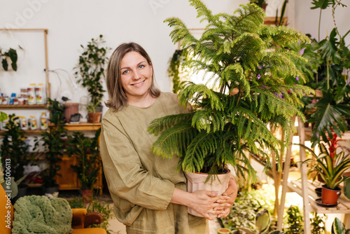 a woman stands in her home greenhouse holding a pot of araucaria