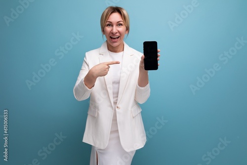 blonde young european woman dressed in a white jacket and dress shows an advertisement on a smartphone