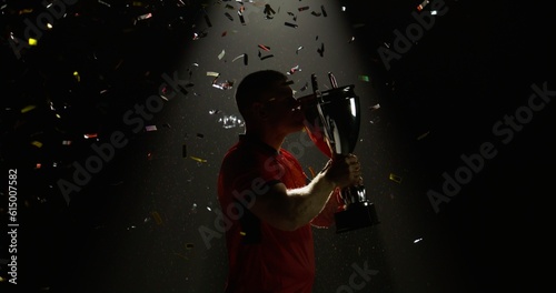 Silhouette of Caucasian male rugby player raising a trophy above head against bright light and falling confetti. Super slow motion, shot on RED cinema camera
