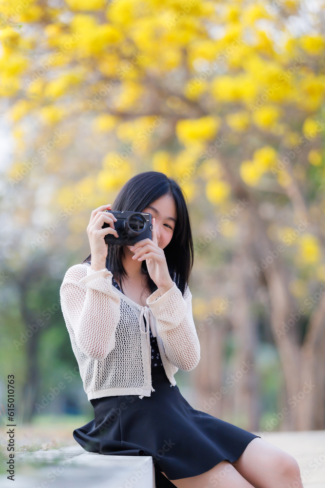 Portrait cute smiles Asian of attractive young teenage girl a holding the camera in blooming Yellow Golden Tabebuia Chrysotricha flowers with the park in spring day at Evening background in Thailand. Portrait cute smiles Asian of attractive young teenage girl a holding the camera in blooming Yellow Golden Tabebuia Chrysotricha flowers with the park in spring day at Evening background in Thailand.