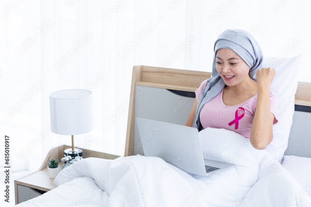 An Asian women disease mammary cancer patient with pink ribbon wearing headscarf After treatment to chemotherapy with working business at laptop on bed In the bedroom at the house, healthcare, medicin An Asian women disease mammary cancer patient with pink ribbon wearing headscarf After treatment to chemotherapy with working business at laptop on bed In the bedroom at the house, healthcare, medicin